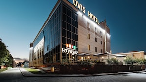 A modern hotel with a prominent 'OVIS HOTEL' sign, a restaurant named 'Voyager' on the ground floor, and a well-lit entrance.
