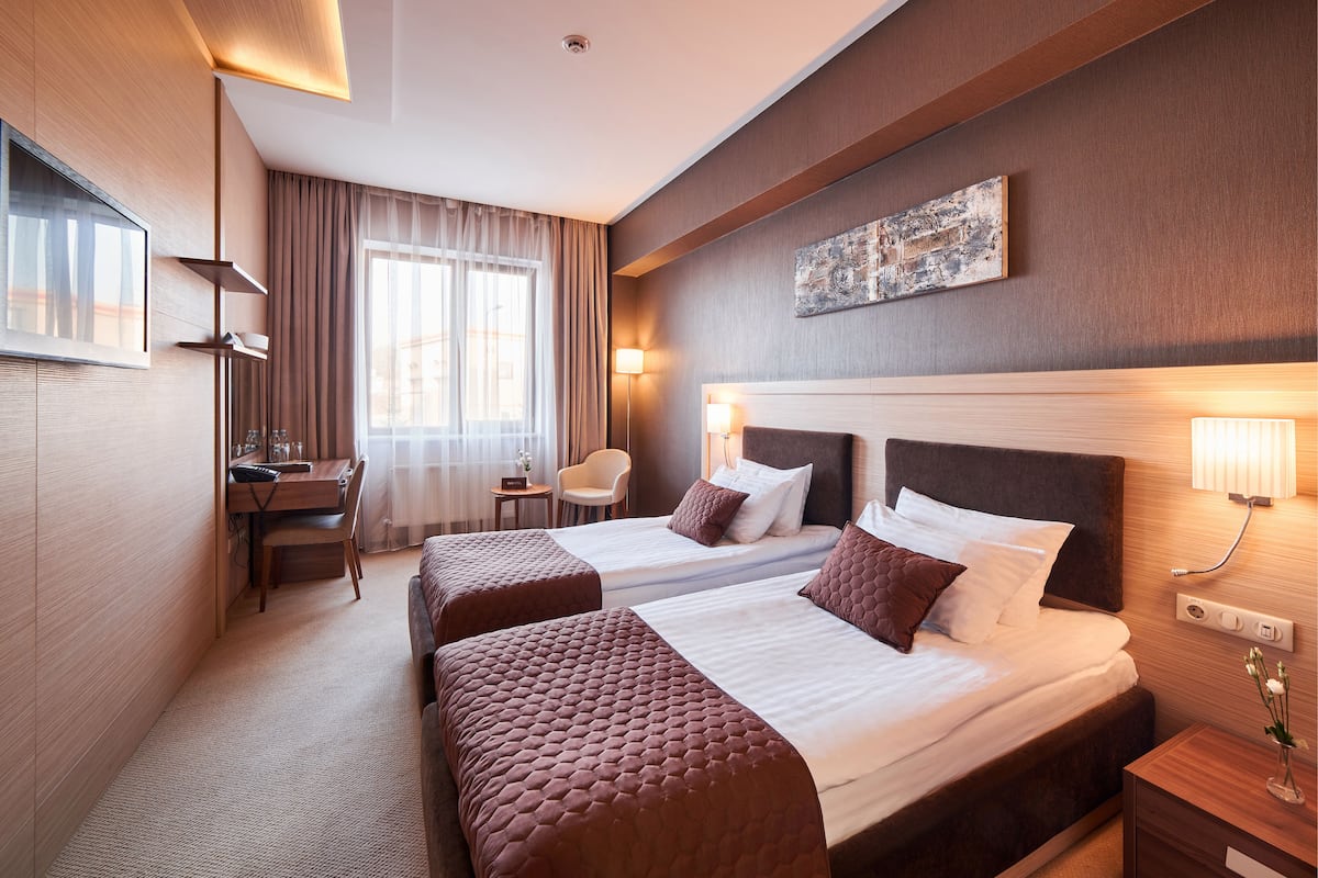 A hotel room with two beds, a desk, a chair, and a lamp.
