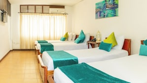 A hotel room with four single beds, each with a teal bedspread and pillows, a wooden headboard, a bedside table with a lamp, and a window with curtains. - Hotel Palmarena Plaza (Santa Marta)