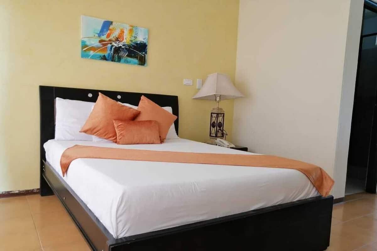 A bed with a black frame, white bedding, and orange pillows.