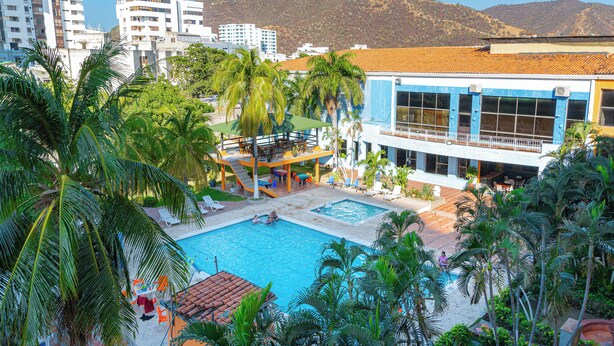 A hotel with a swimming pool, outdoor seating, and palm trees. - Hotel Palmarena Plaza (Santa Marta)