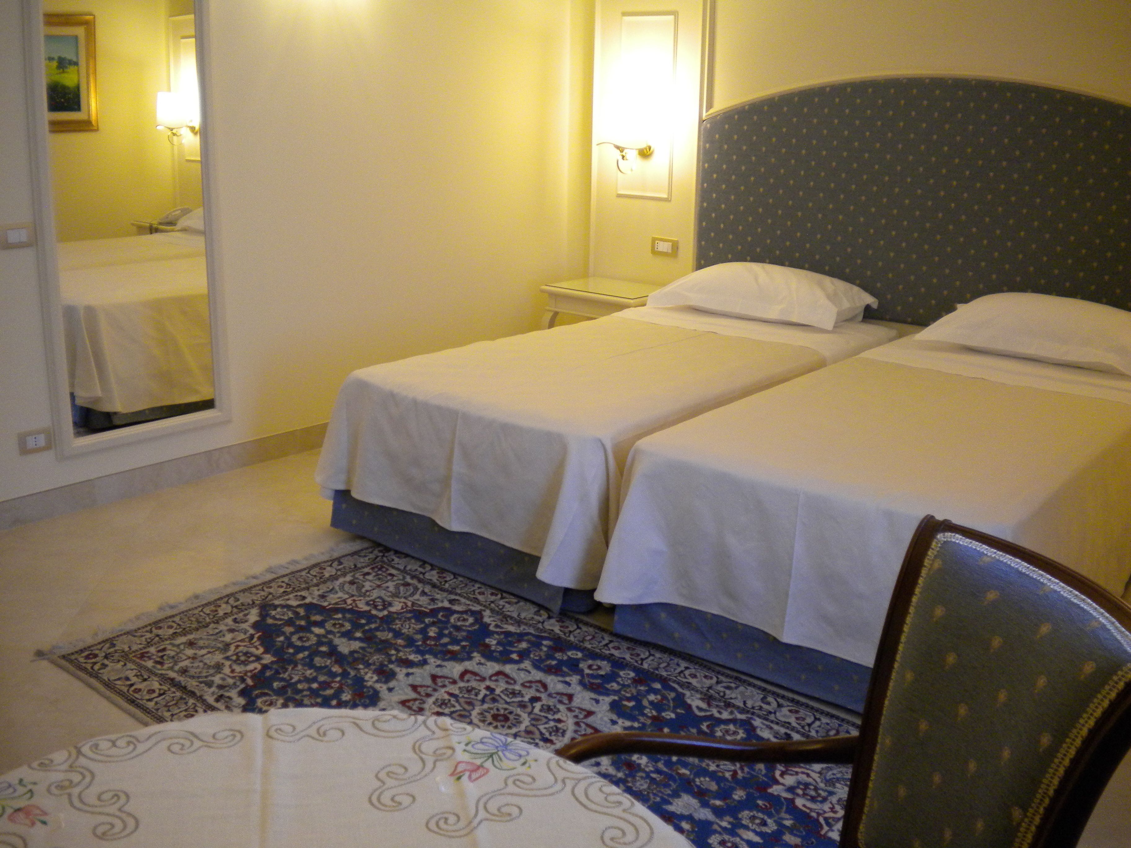 Une chambre d’hôtel avec deux lits simples, une table de chevet, une lampe de chevet, un tapis à motifs et une chaise.