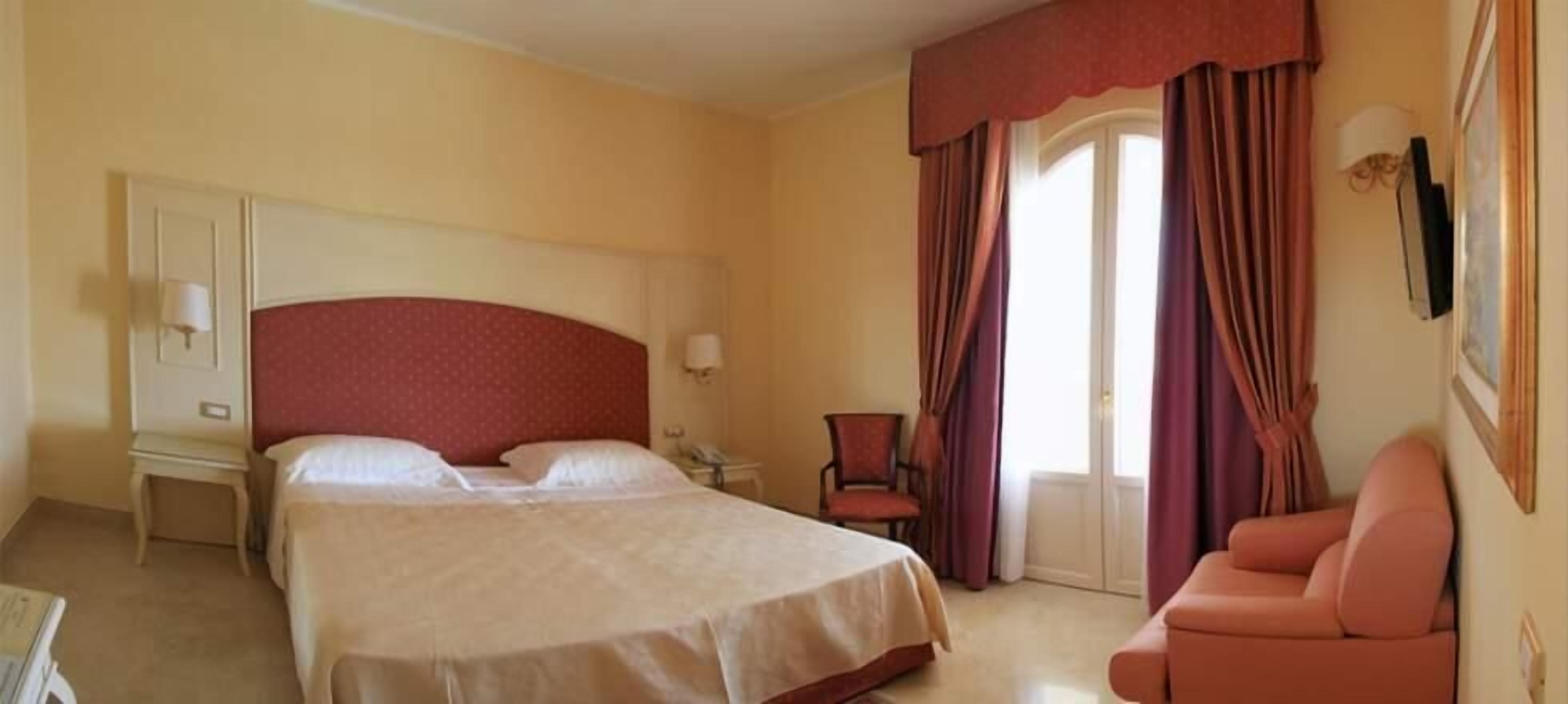 A hotel room with a large bed, a desk, a chair, and a sofa.