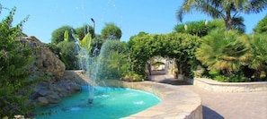 A landscaped garden with a fountain, stone pathway, and tropical plants.