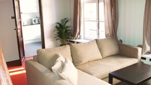 Ein Wohnzimmer mit einem beigen Sofa, einem Couchtisch, einer Zimmerpflanze und einem Fenster mit Vorhängen.
