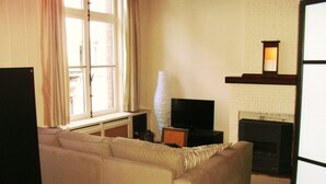 Ein Wohnzimmer mit einer Couch, einem Fernseher, einem Kamin und einem Fenster mit Vorhängen.