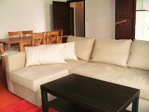A living room with a beige sofa, a black coffee table, and a wooden dining table with chairs.