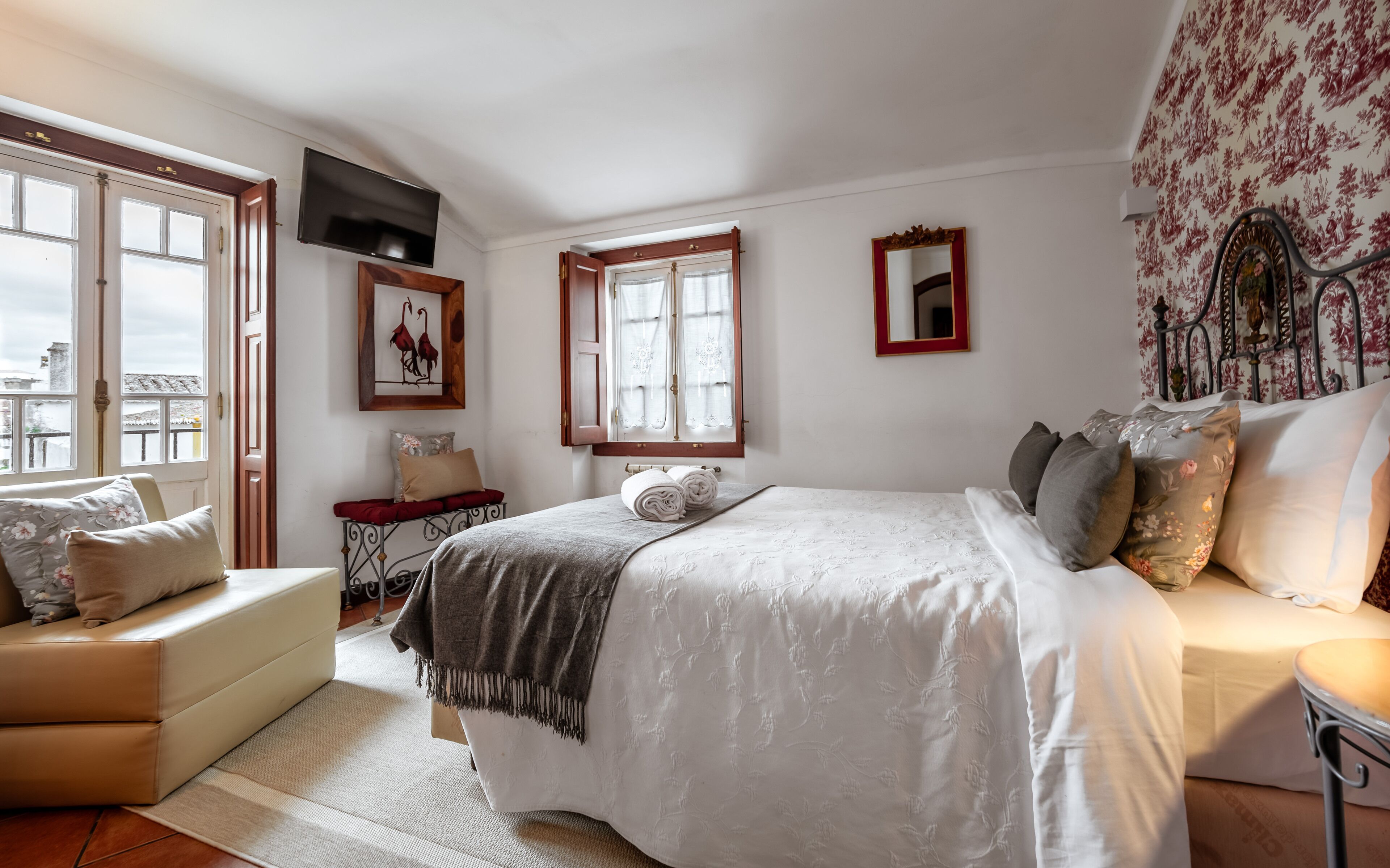 Quarto com cama, sofá, janela, televisão e espelho.