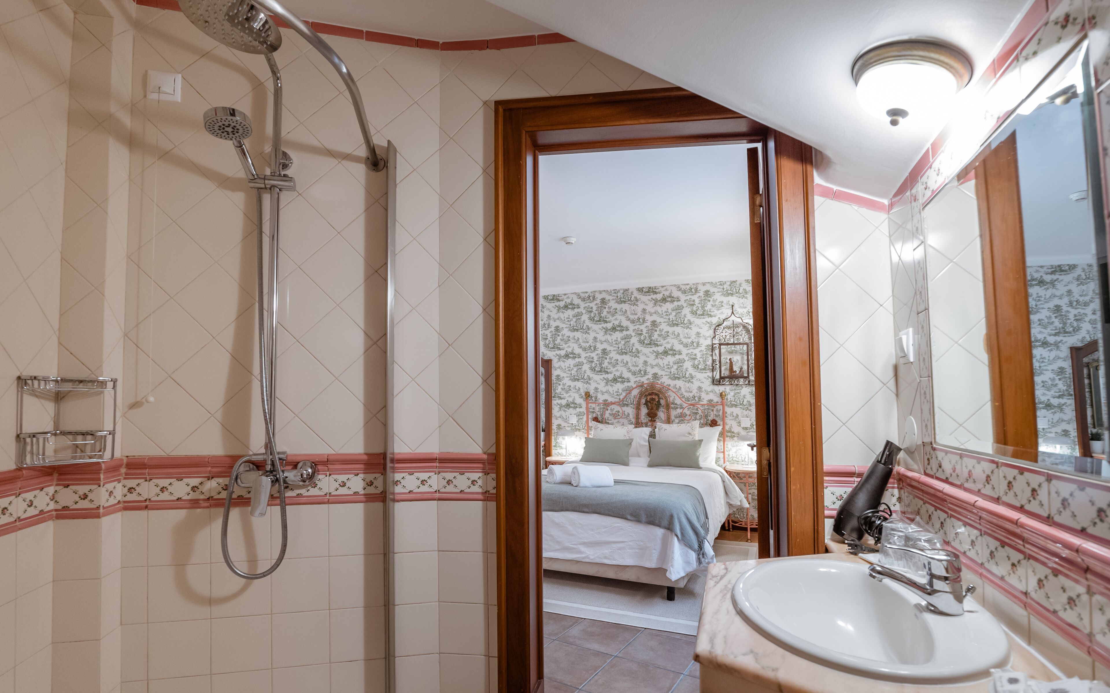 A bathroom with a shower, a sink, and a bed visible through an open door.