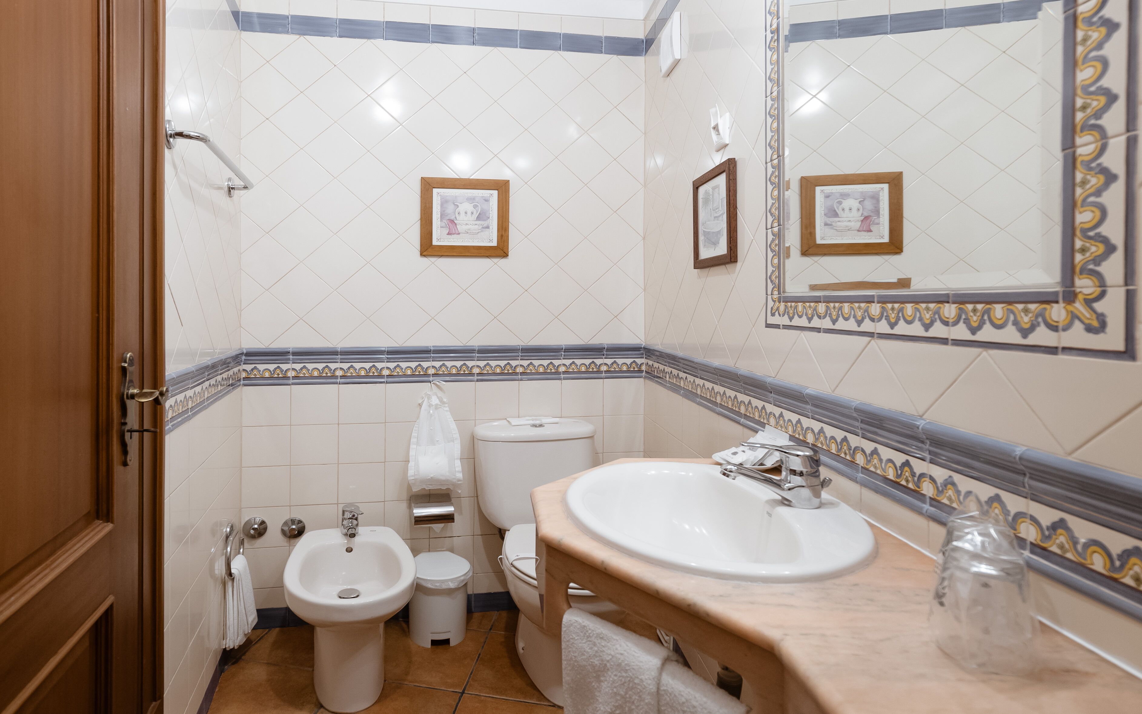 Ein Badezimmer mit Waschbecken, Bidet, Toilette und einem Spiegel mit dekorativen Fliesen.
