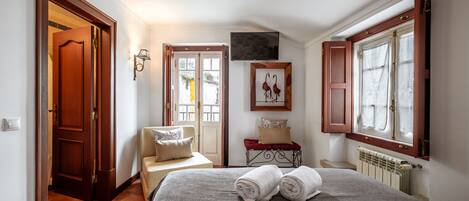 Un dormitorio con cama, una silla, un televisor, una ventana y una puerta.