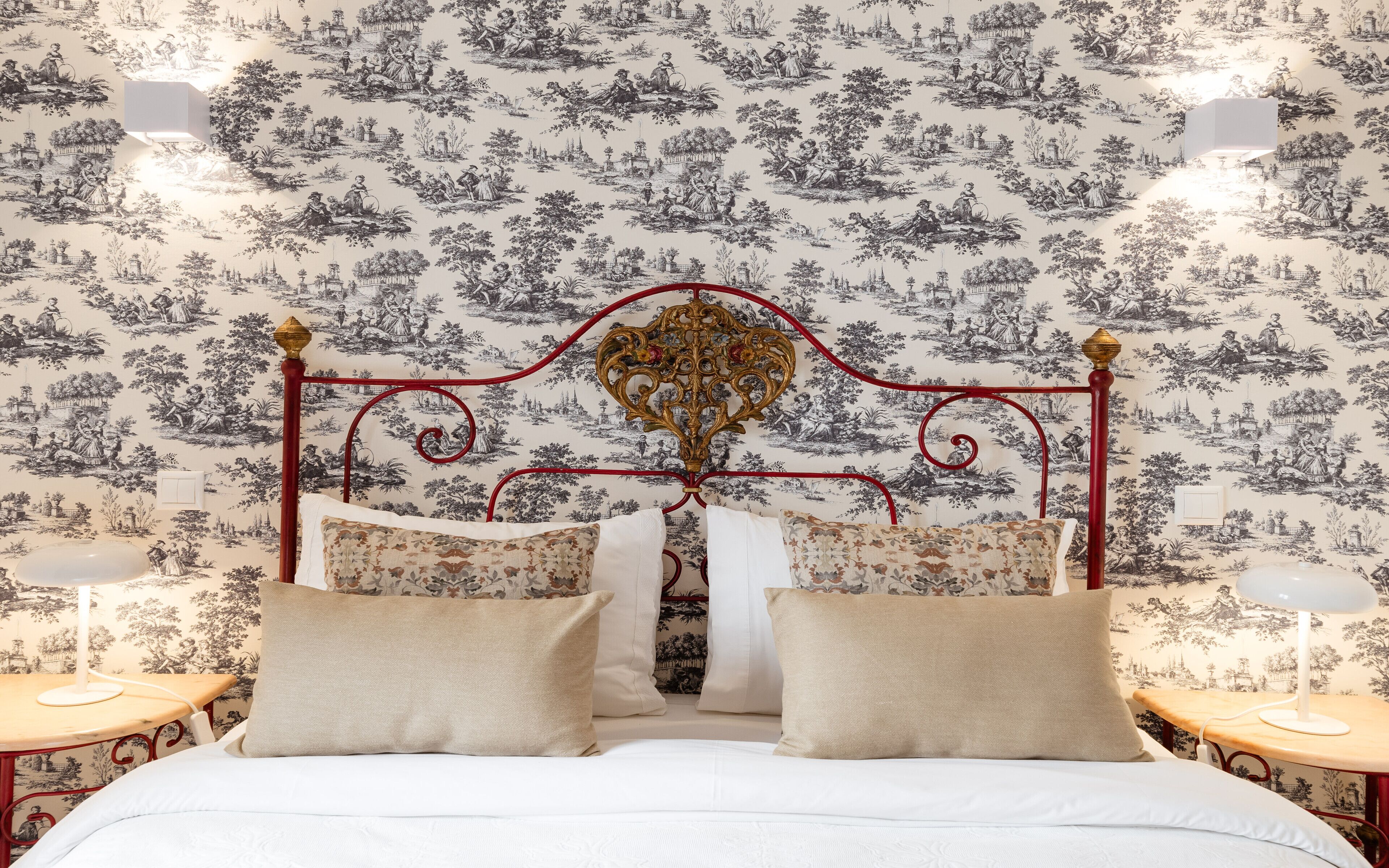 Un dormitorio de diseño clásico, con una cama con cabecera decorativa, dos mesitas de noche y un papel pintado estampado.