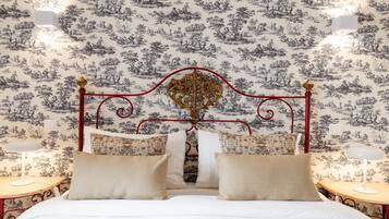 A bedroom with a classic design, featuring a bed with a decorative headboard, two bedside tables, and a patterned wallpaper.