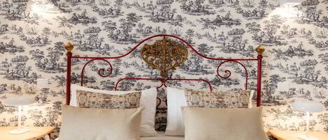 Un dormitorio de diseño clásico, con una cama con cabecera decorativa, dos mesitas de noche y un papel pintado estampado.