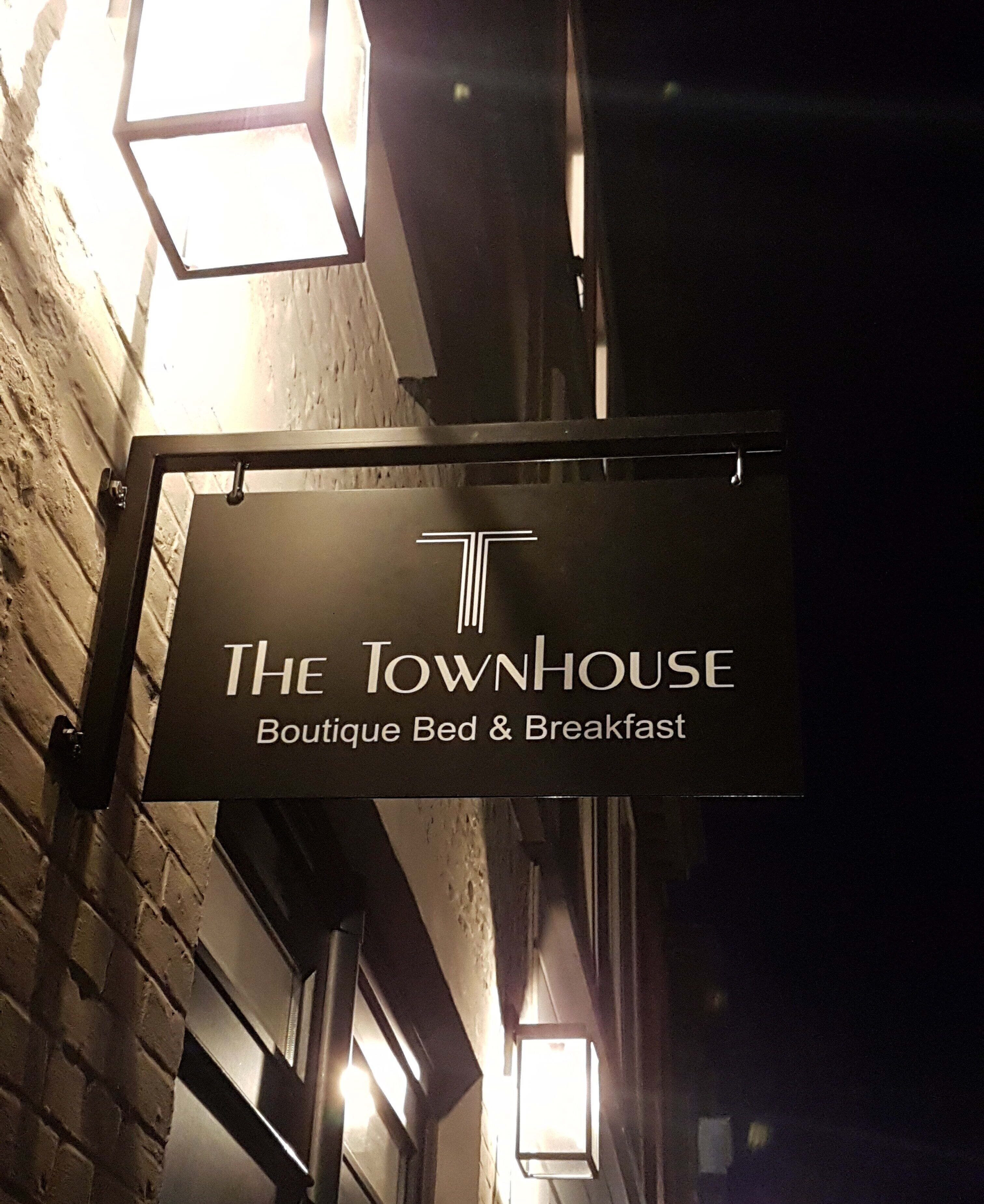 A sign for 'The Townhouse Boutique Bed & Breakfast' mounted on a brick wall.