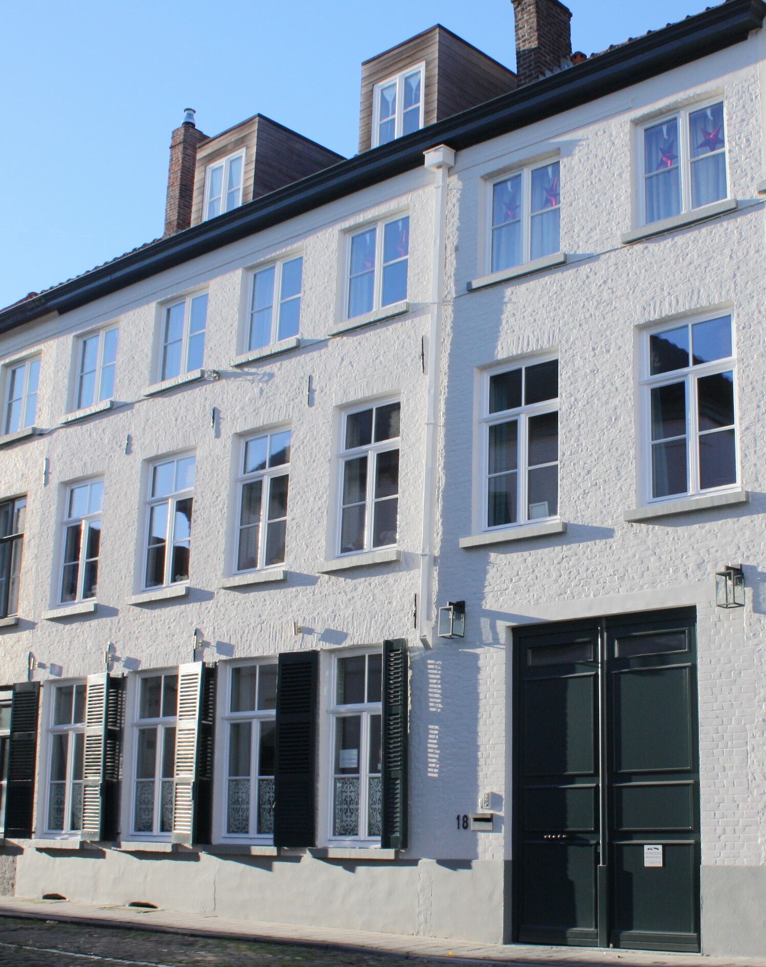 A row of white buildings with multiple windows and doors, some with shutters.