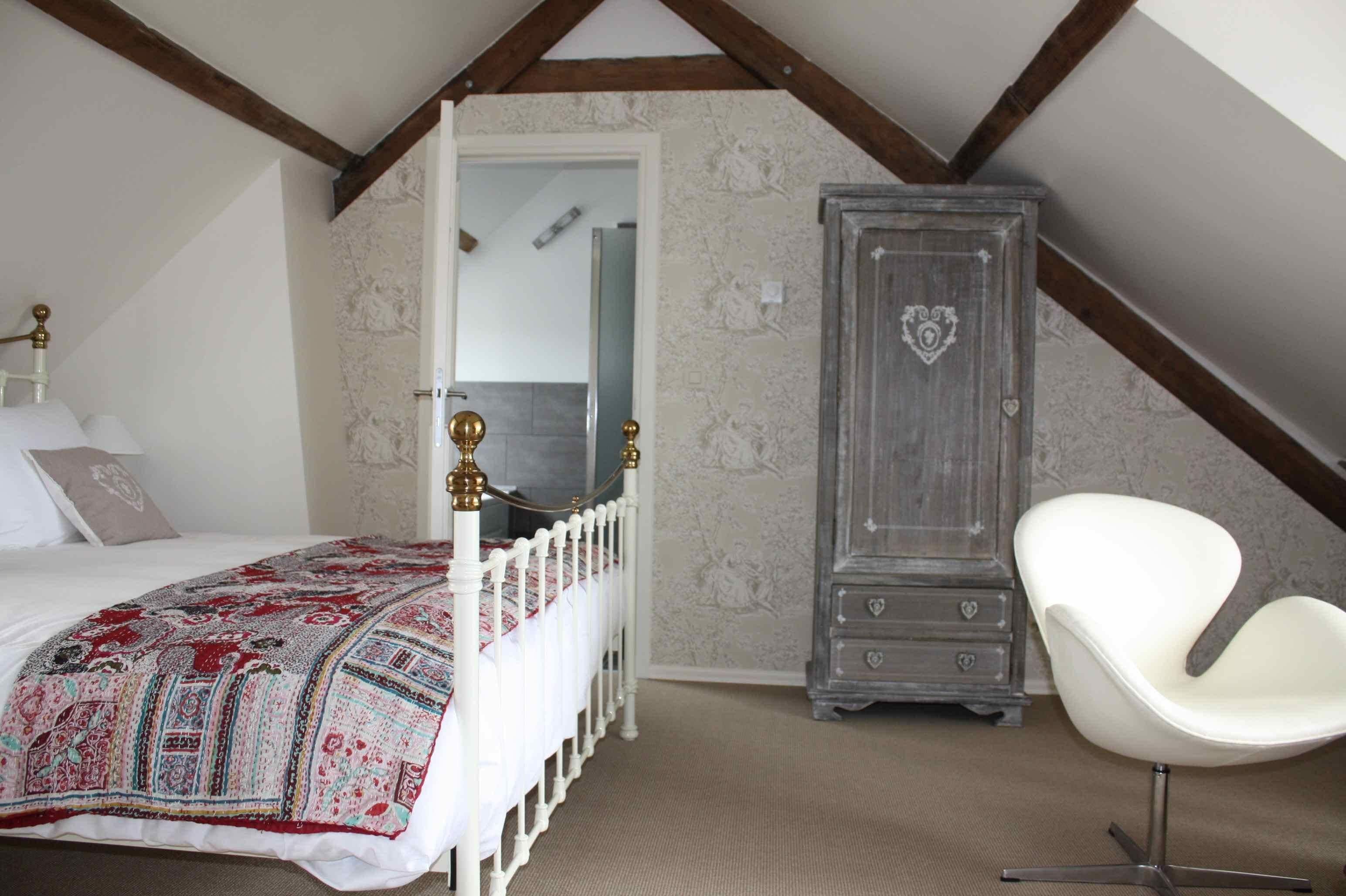 A bedroom with a bed, a white chair, and a wardrobe.