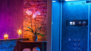 A modern bathroom with a brick wall, a blue shower enclosure, a potted orchid, and neatly folded towels on a shelf. - Di Sabatino Resort (Ascoli Piceno)