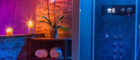 Un baño moderno con pared de ladrillo, recinto de ducha azul, orquídea en maceta y toallas dobladas prolijamente en un estante.