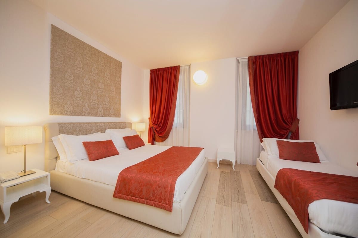 A hotel room with two beds, a large wall clock, and a flat-screen TV.