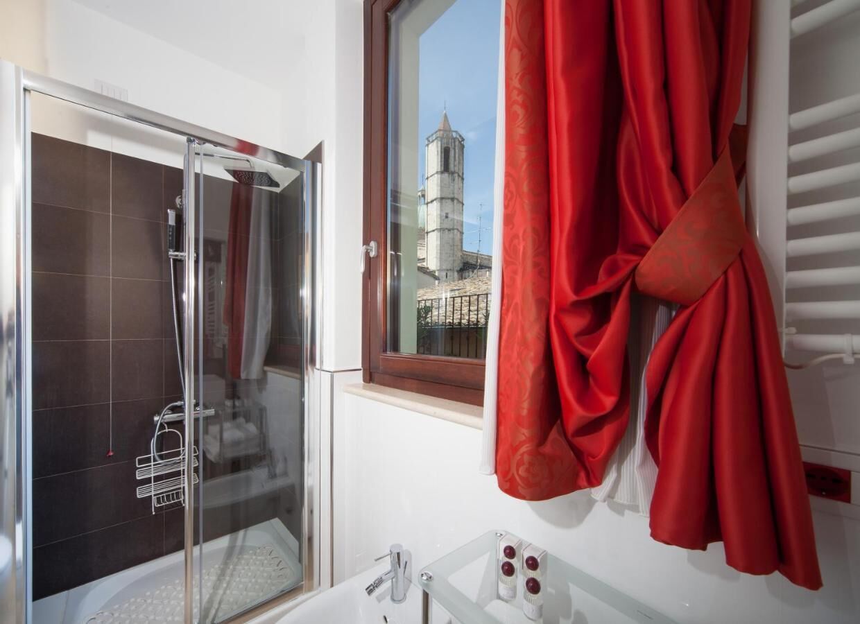 A bathroom with a glass shower enclosure, a window with a view of a tower, and a red towel hanging on the wall.