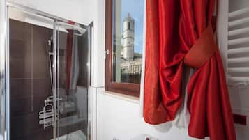 A bathroom with a glass shower enclosure, a window with a view of a tower, and a red towel hanging on the wall.