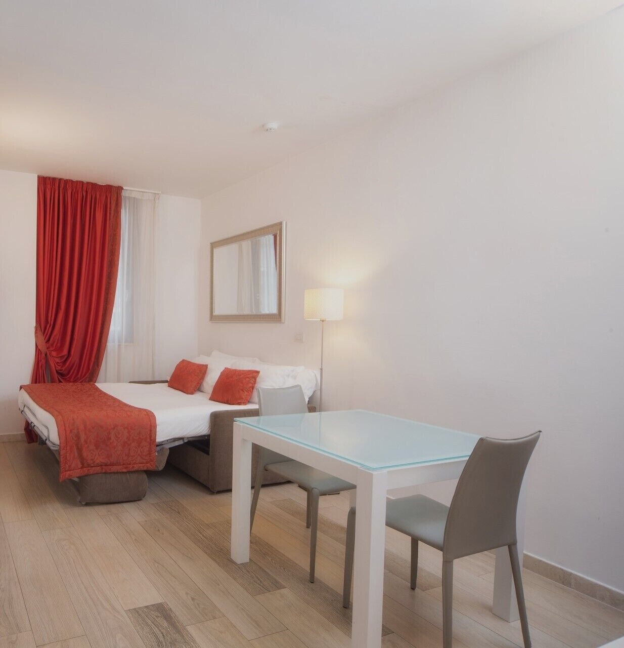 A hotel room with a bed, two bedside tables, a desk, a chair, and a lamp.