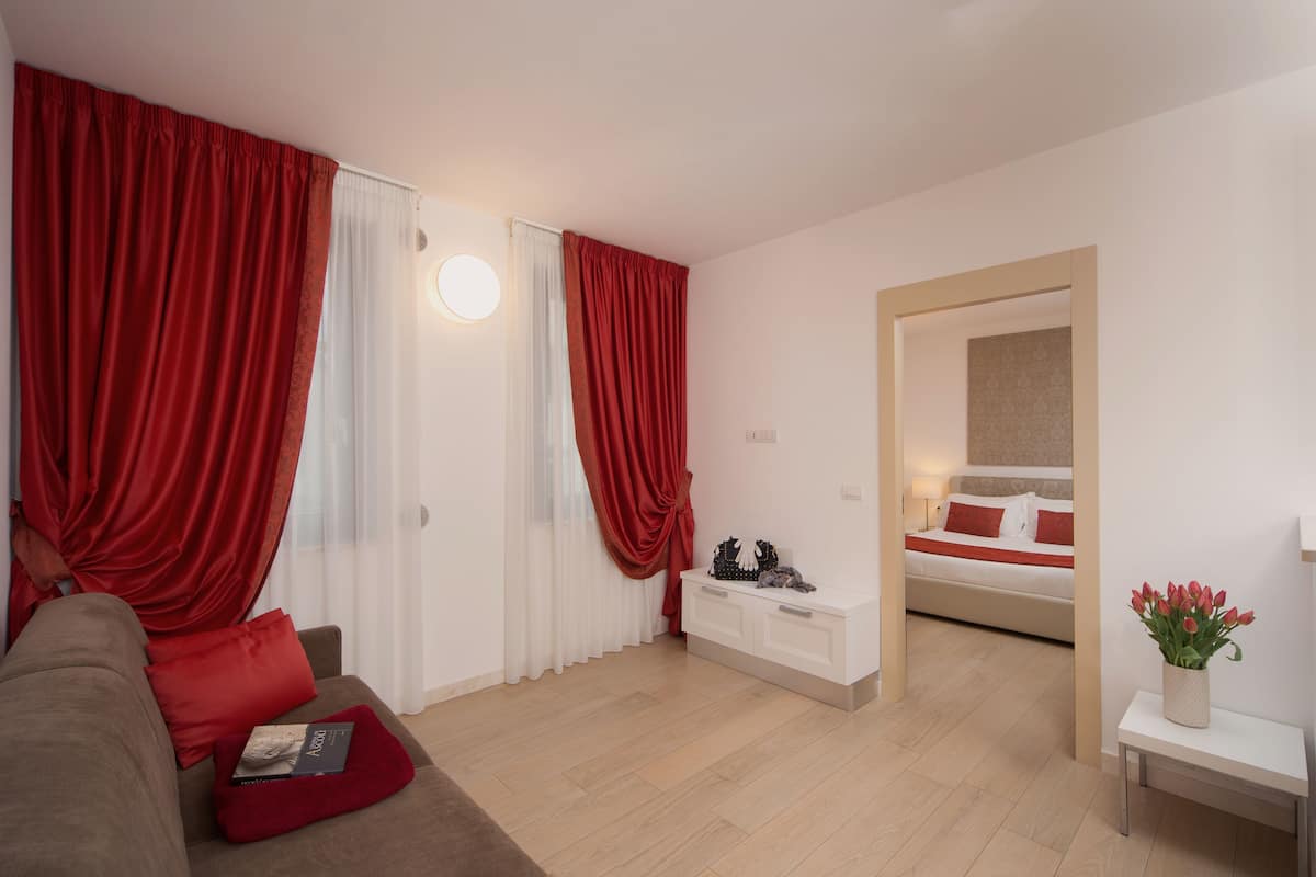 A modern living room with a sofa, a white console table, and a bed with red bedding.
