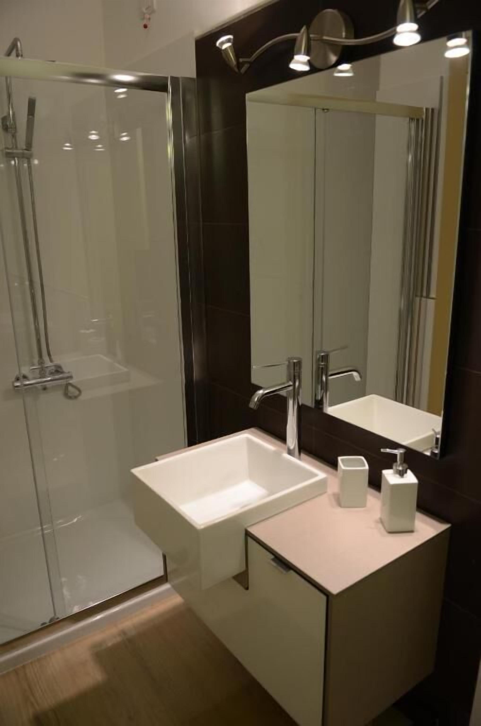 Un baño moderno con cabina de ducha de vidrio, un lavabo blanco y un espejo grande sobre el mueble.