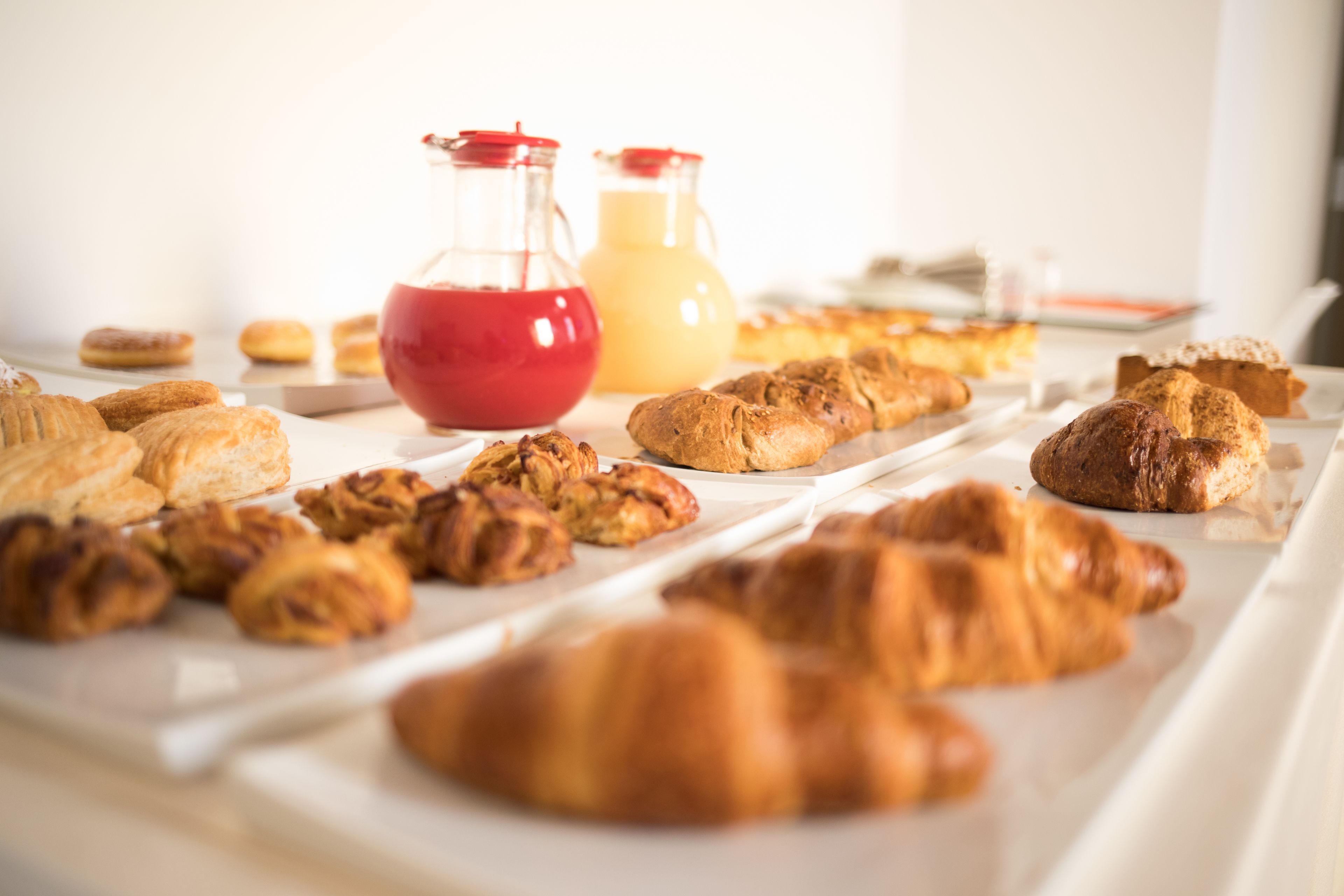 A breakfast buffet with pastries, croissants, and two pitchers of beverages.