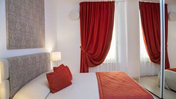 A hotel room with a bed, a bedside lamp, a mirror, and red curtains.