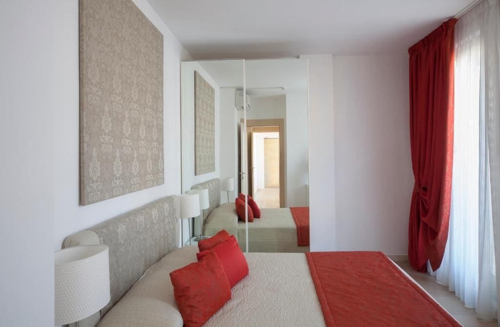 A hotel room with a large bed, two bedside tables, a mirror, and a red curtain.