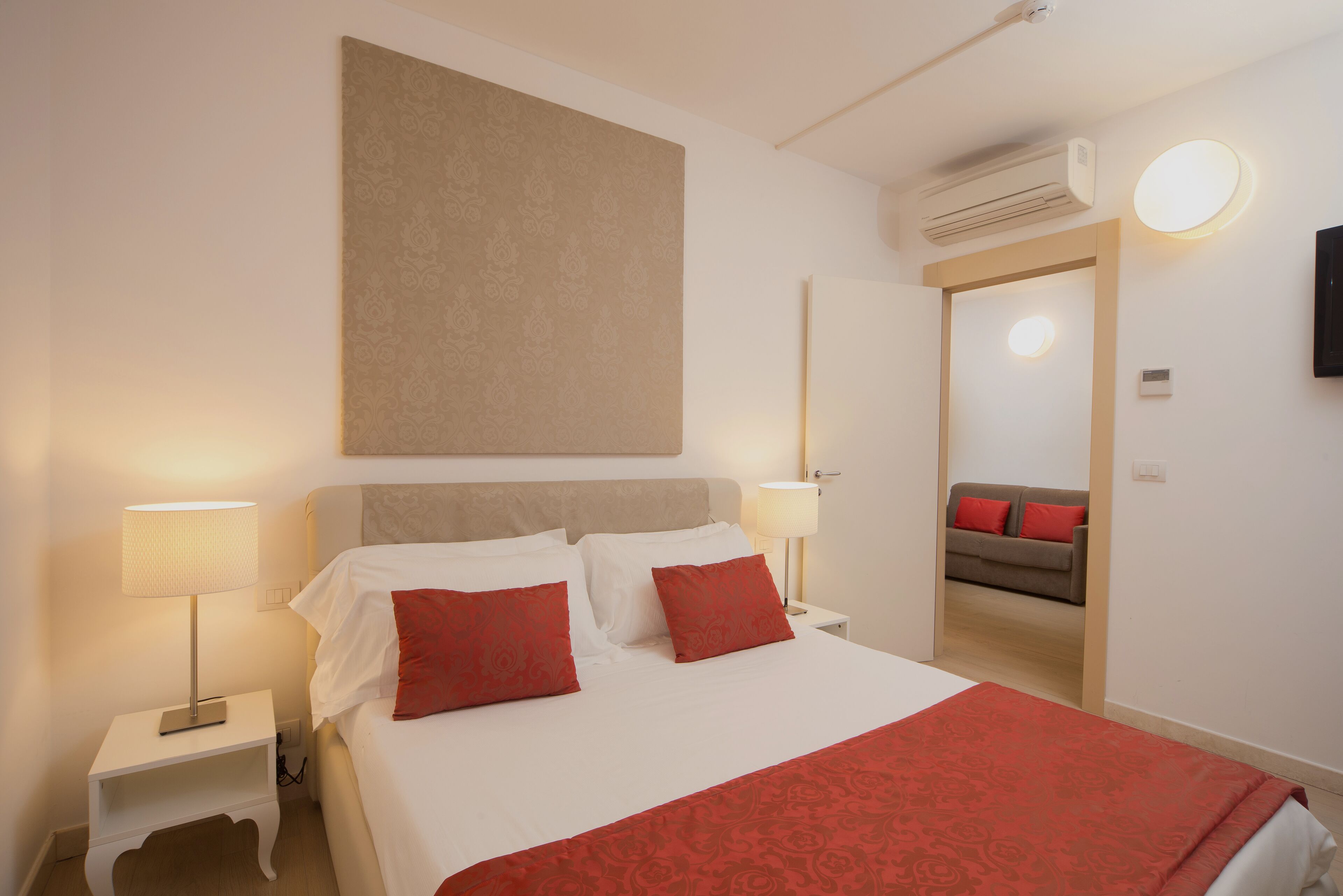 Een hotelkamer met een bed, twee bedlampen, een wandairconditioner en een bank in de aangrenzende kamer.