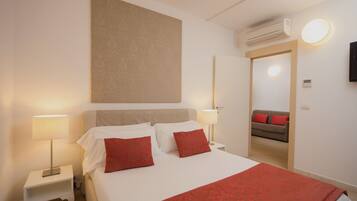 Habitació d'hotel amb un llit, dues làmpades de nit, aire condicionat fixat a la paret i un sofà a l'habitació següent.