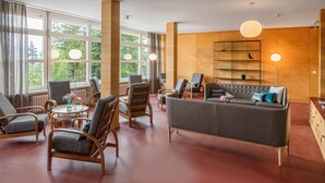 A modern living room with a grey sofa, wooden chairs, and a large window with curtains. - Youth Hostel Crans-Montana (Crans-Montana)