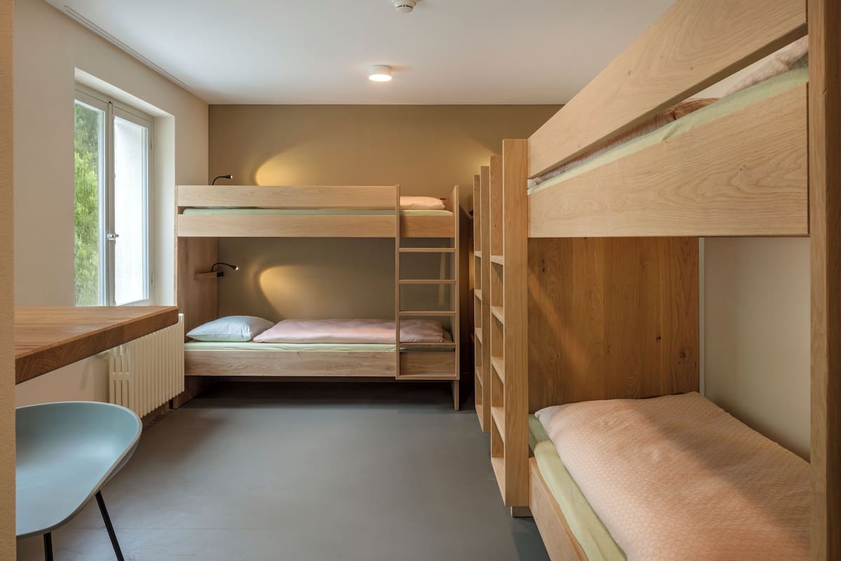 A bunk bed room with a desk and chair, a window, and a radiator.
