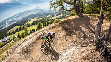 A mountain biker on a dirt trail with a view of a valley and distant mountains.