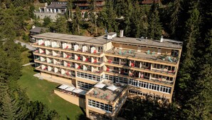A multi-story hotel with balconies, surrounded by dense forest. - Youth Hostel Crans-Montana (Crans-Montana)