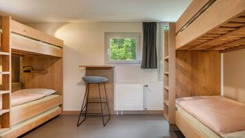 Habitación pequeña con dos literas, un taburete, una ventana que da a zonas verdes y un radiador.