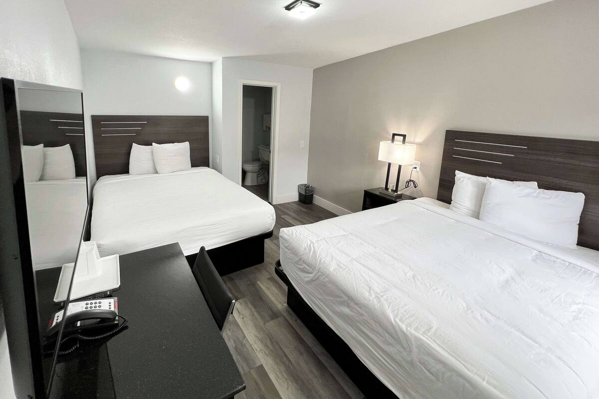 A hotel room with two beds, a desk, a lamp, and a mirror.