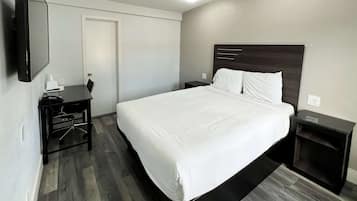 A modern hotel room with a large bed, a desk, and a flat-screen TV.