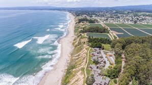 Vue aérienne d’une zone côtière comprenant une plage, des immeubles résidentiels et des champs agricoles.