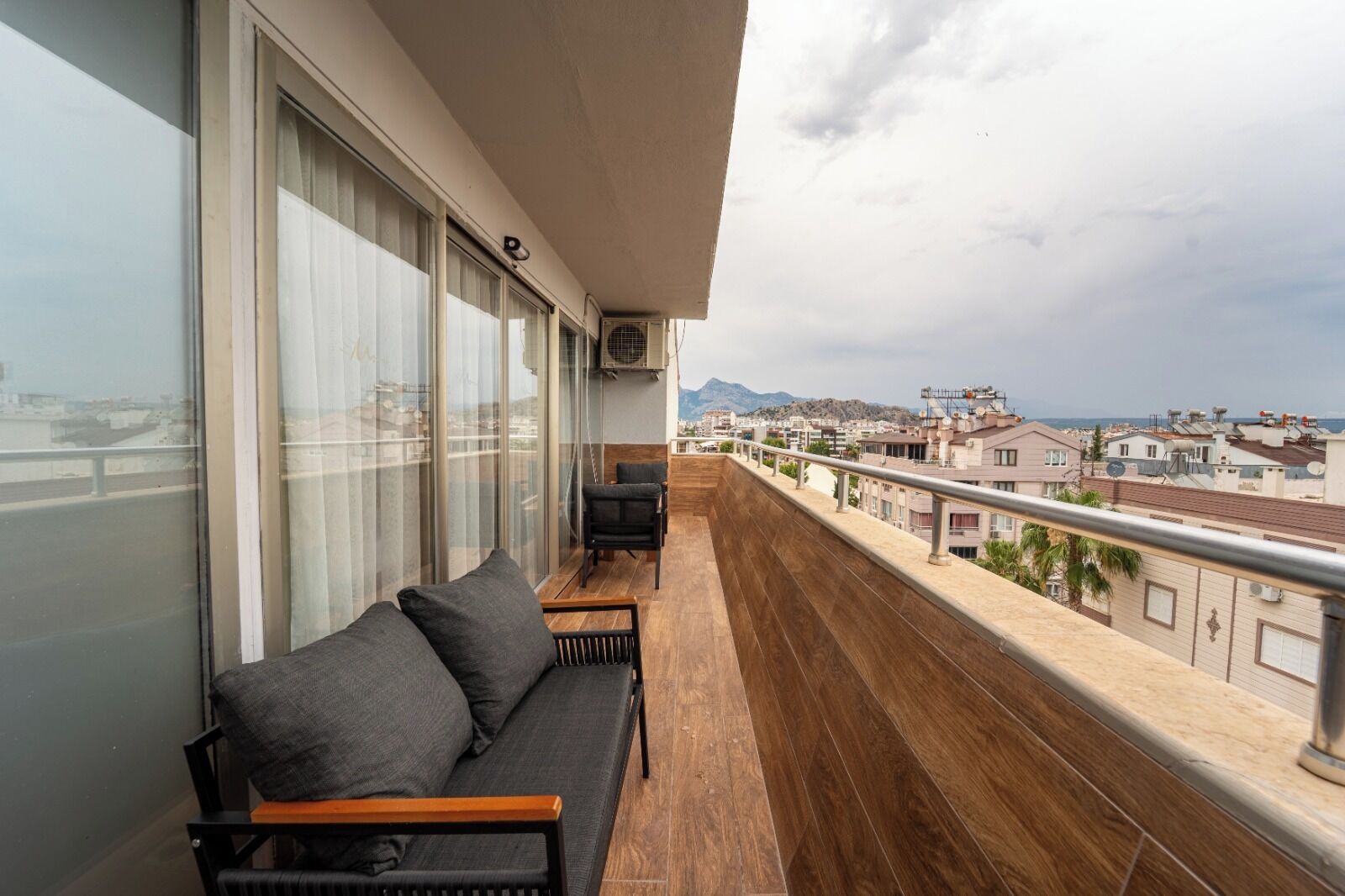 A balcony with a sofa and chairs, a view of the cityscape, and a railing.