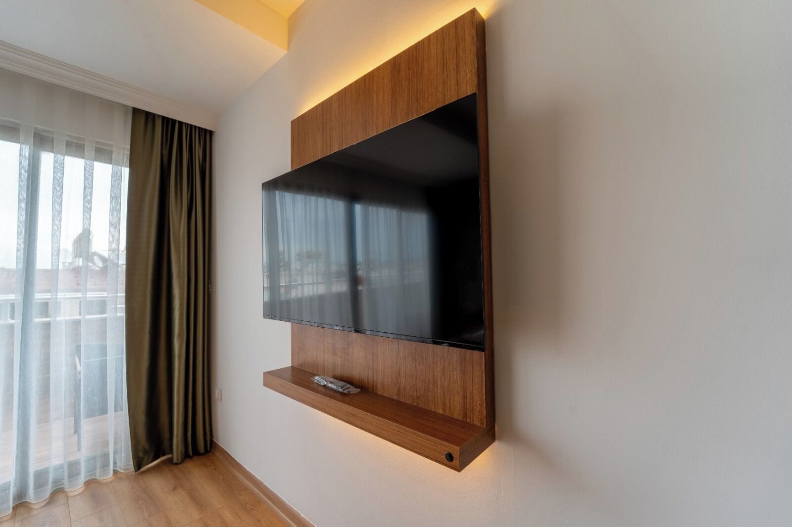 A modern wall-mounted TV with a wooden panel and a shelf below.