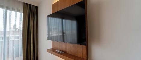 A modern wall-mounted TV with a wooden panel and a shelf below.