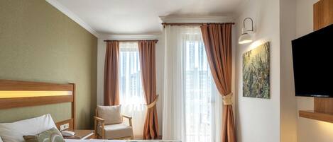 A hotel room with a bed, a chair, a TV, and curtains.