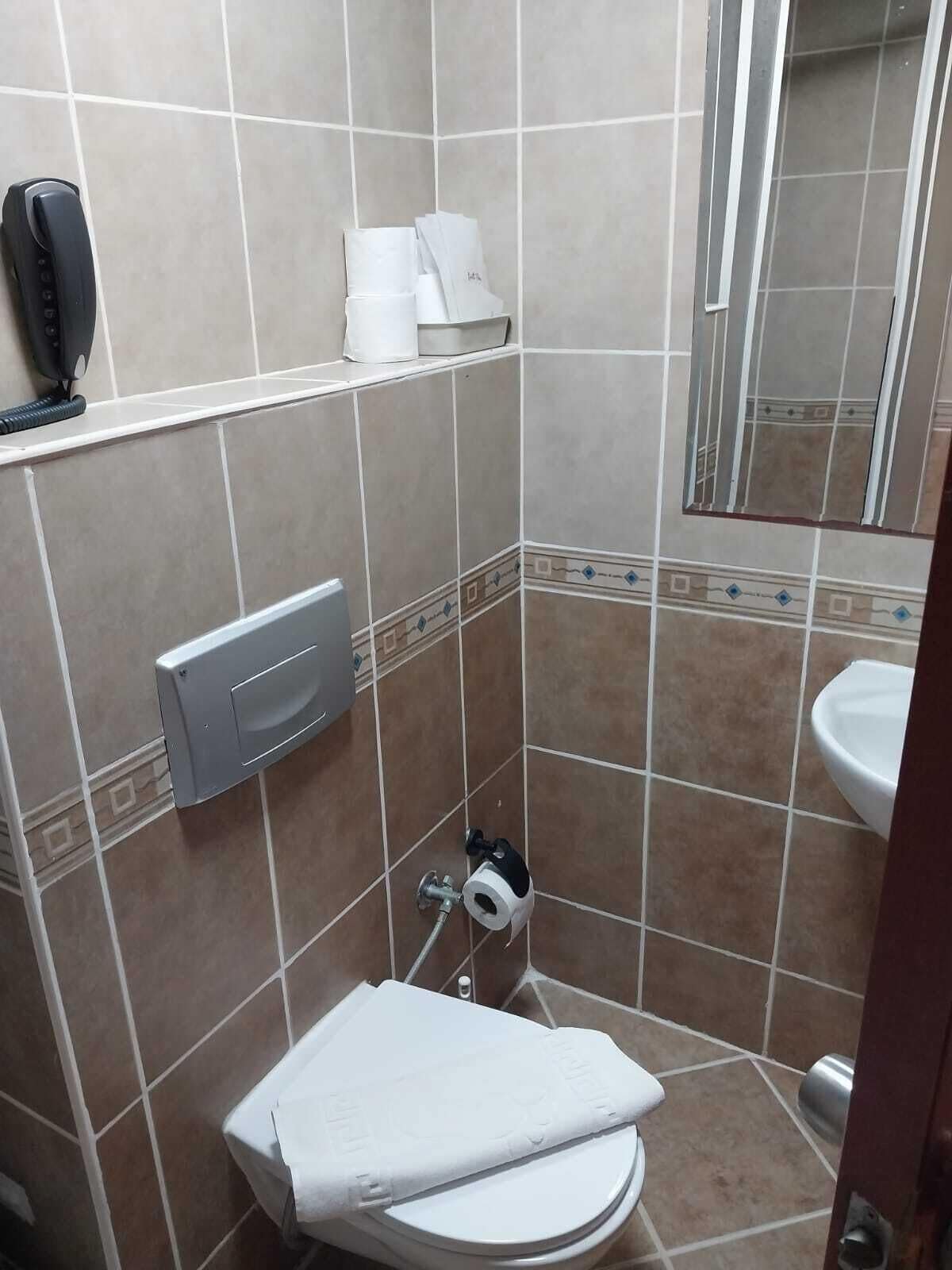 Un baño pequeño con inodoro, secamanos, dispensador de toallas de papel y espejo.