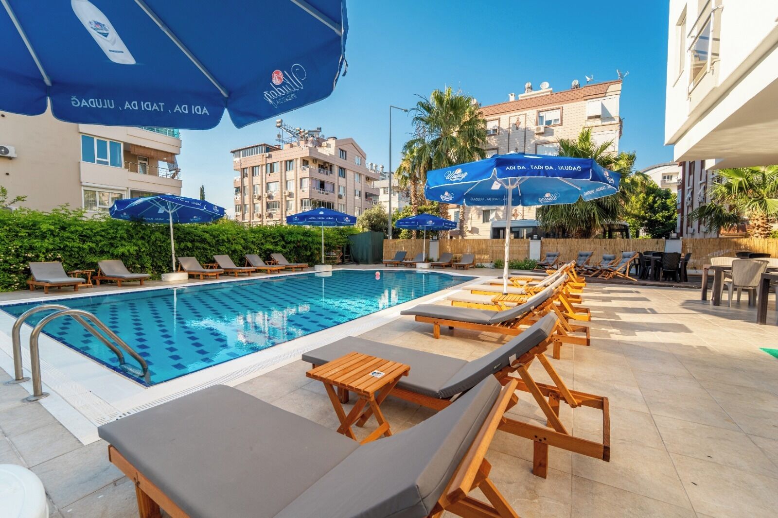 Una piscina con sillones de playa y sombrillas, rodeada de edificios.