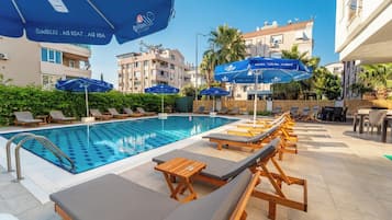 Una piscina con sillones de playa y sombrillas, rodeada de edificios.