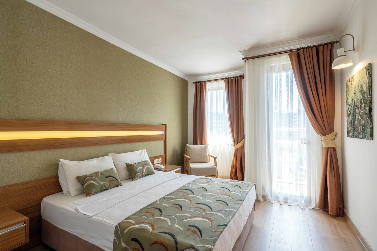 Een hotelkamer met een bed, een stoel, een nachtkastje en een raam met gordijnen.